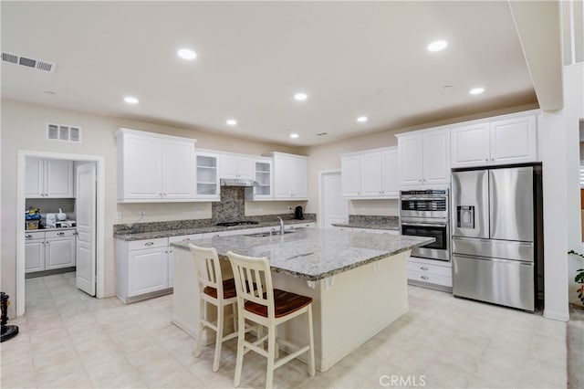 kitchen with white cabinets, a center island with sink, appliances with stainless steel finishes, a breakfast bar area, and light stone countertops