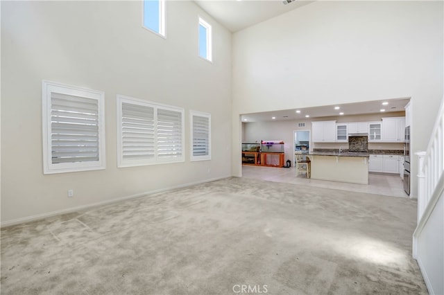 unfurnished living room with sink, a towering ceiling, and light colored carpet