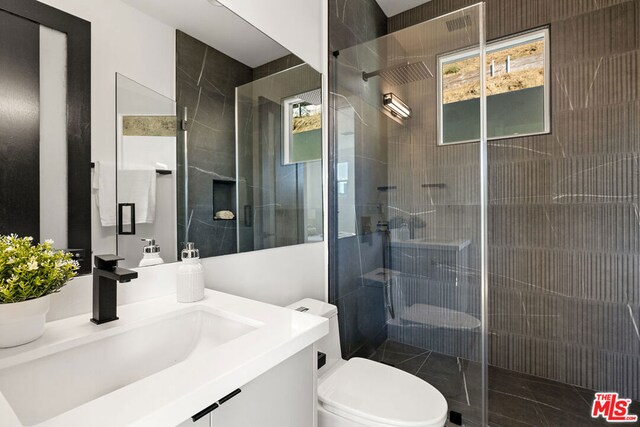 bathroom featuring a shower with door, vanity, and toilet