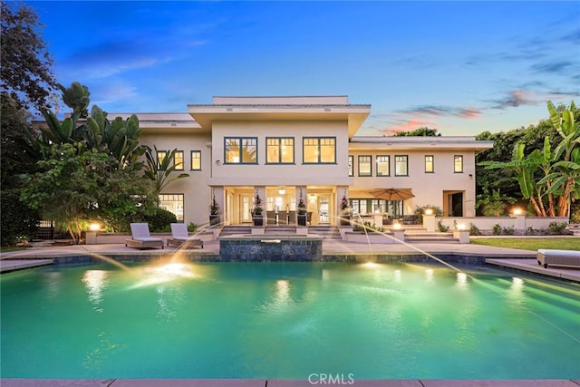 back house at dusk featuring a swimming pool with hot tub and a patio