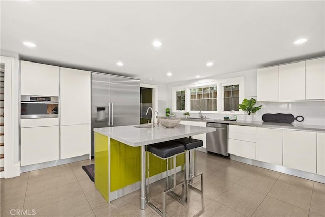 kitchen featuring appliances with stainless steel finishes, a kitchen breakfast bar, sink, a center island with sink, and white cabinetry