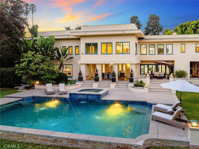 back house at dusk featuring pool water feature, a pool with hot tub, and a patio