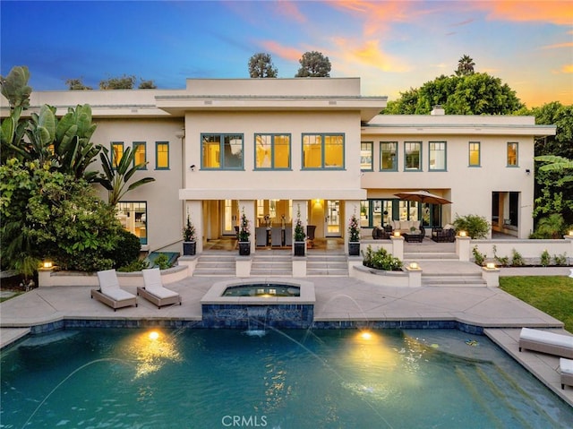 back house at dusk with a patio area, pool water feature, and a pool with hot tub