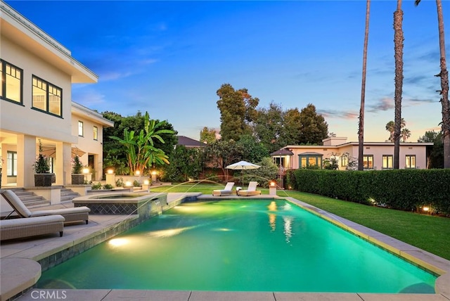 pool at dusk with an in ground hot tub, pool water feature, and a lawn