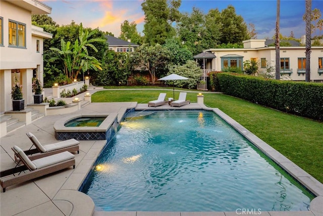 pool at dusk featuring a lawn, pool water feature, and an in ground hot tub