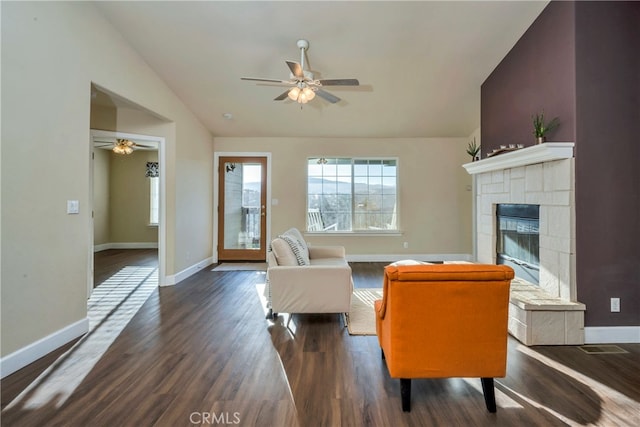 living room with lofted ceiling, a tiled fireplace, ceiling fan, and dark wood-type flooring