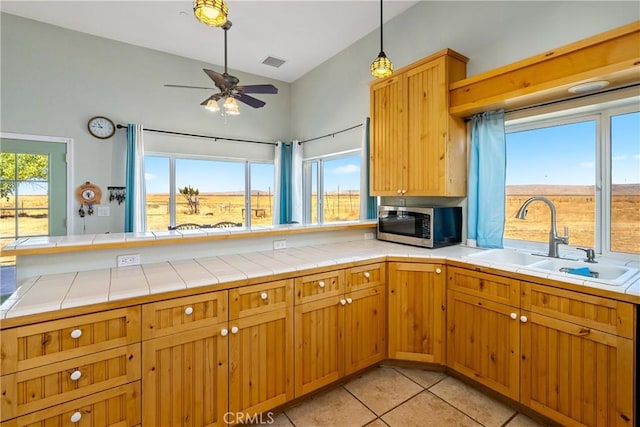 kitchen with tile countertops, sink, light tile patterned floors, ceiling fan, and kitchen peninsula