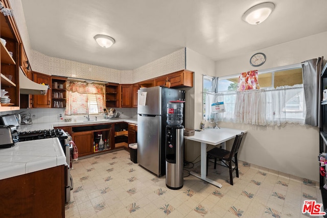 kitchen with sink, appliances with stainless steel finishes, tasteful backsplash, tile counters, and kitchen peninsula