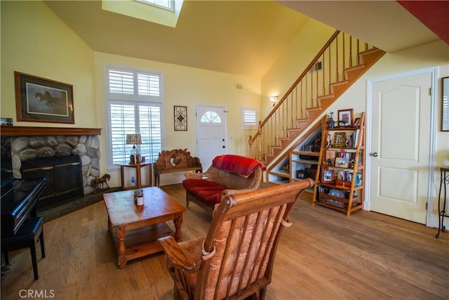 living room featuring wood-type flooring, a stone fireplace, a skylight, and a high ceiling