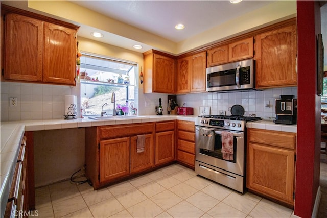 kitchen with appliances with stainless steel finishes, decorative backsplash, light tile patterned flooring, tile counters, and sink