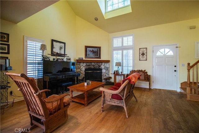 living room featuring wood-type flooring, a fireplace, high vaulted ceiling, and a skylight