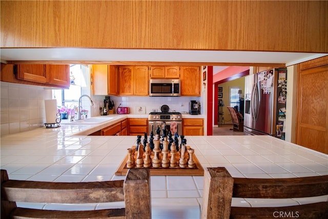 kitchen featuring decorative backsplash, kitchen peninsula, stainless steel appliances, tile countertops, and sink