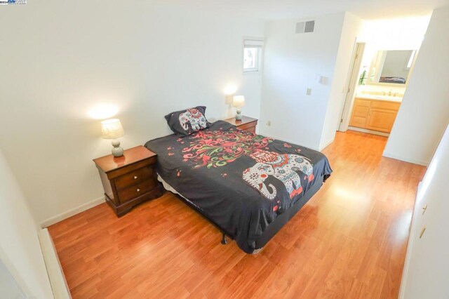 bedroom with connected bathroom, hardwood / wood-style flooring, and sink