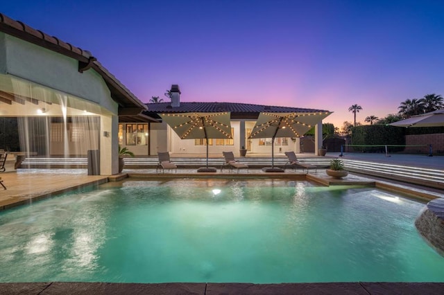 pool at dusk with a patio area and pool water feature