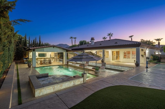 back house at dusk featuring a pool with hot tub and a patio