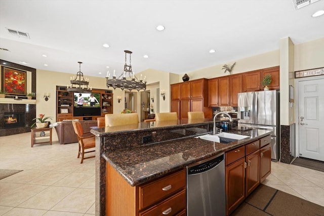 kitchen with pendant lighting, stainless steel appliances, an island with sink, a high end fireplace, and sink