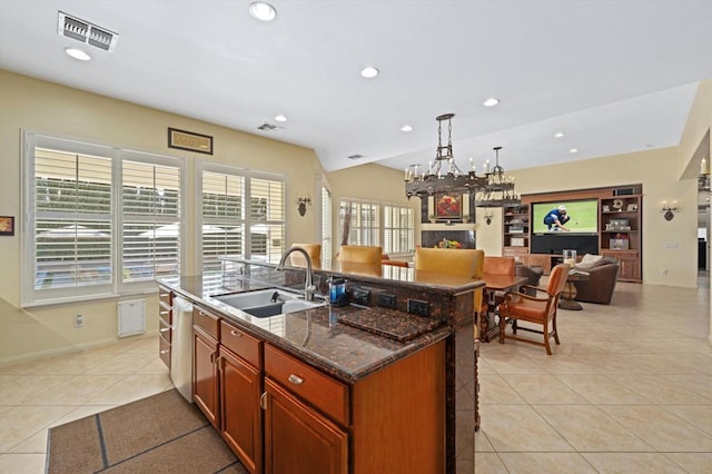 kitchen featuring sink, light tile patterned floors, an island with sink, dark stone counters, and built in shelves