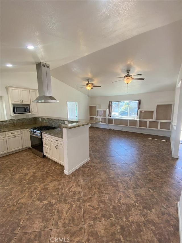 kitchen featuring white cabinetry, appliances with stainless steel finishes, lofted ceiling, dark stone counters, and wall chimney exhaust hood