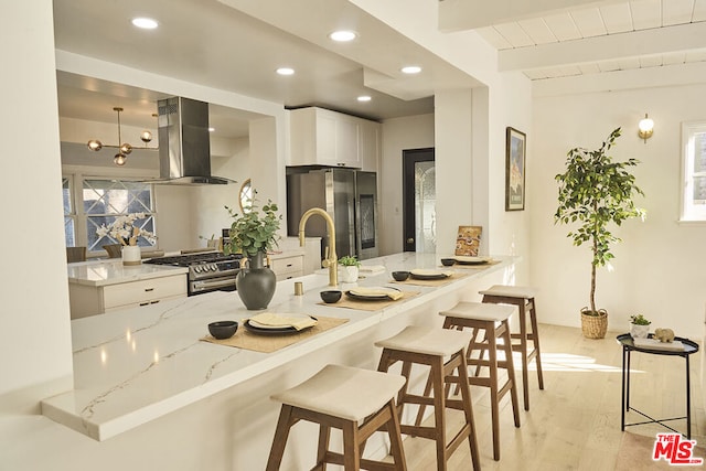 kitchen with light hardwood / wood-style flooring, light stone countertops, island range hood, white cabinetry, and stainless steel appliances