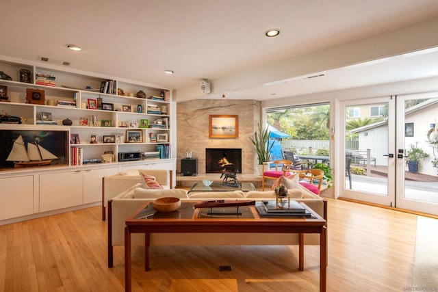 living room featuring light wood-type flooring, built in shelves, french doors, and a fireplace