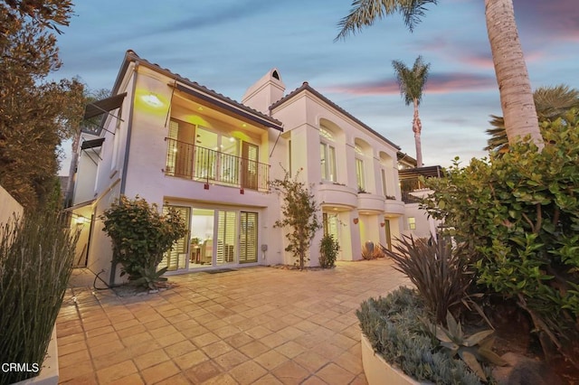 back of property at dusk with a balcony, a patio area, and stucco siding