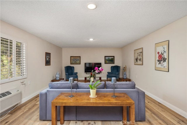 living room featuring an AC wall unit, light hardwood / wood-style floors, and a textured ceiling