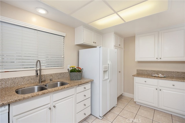 kitchen with white refrigerator with ice dispenser, sink, white cabinetry, light tile patterned floors, and light stone countertops