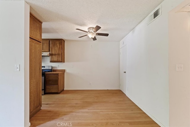 kitchen featuring light wood-type flooring, stainless steel range oven, a textured ceiling, and custom range hood