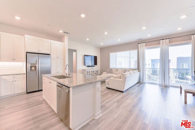 kitchen with light hardwood / wood-style floors, an island with sink, white cabinets, stainless steel appliances, and sink