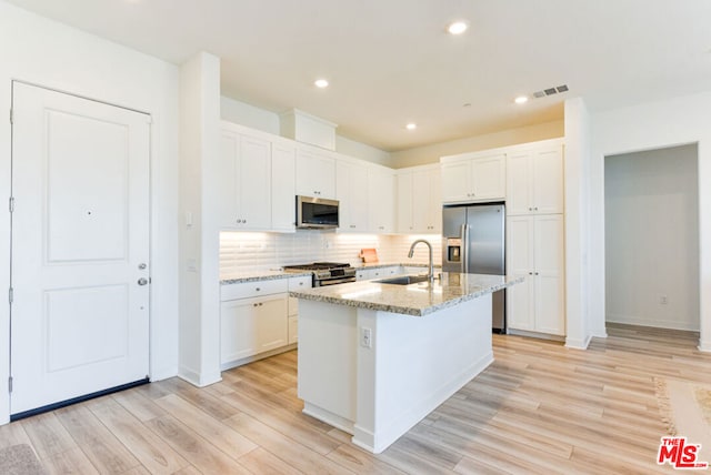 kitchen featuring a center island with sink, white cabinetry, appliances with stainless steel finishes, light stone countertops, and light hardwood / wood-style floors