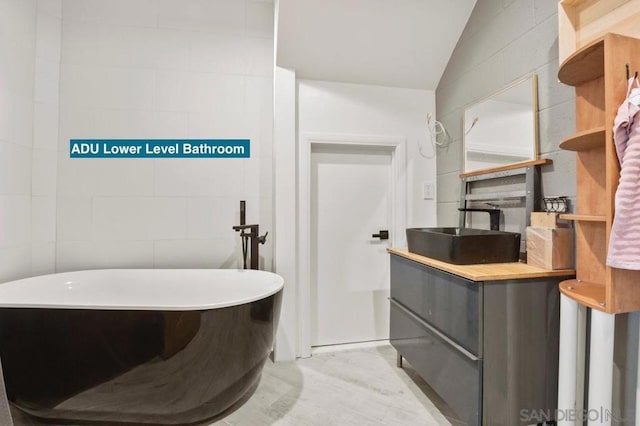 bathroom with tile walls, lofted ceiling, a bath, and vanity