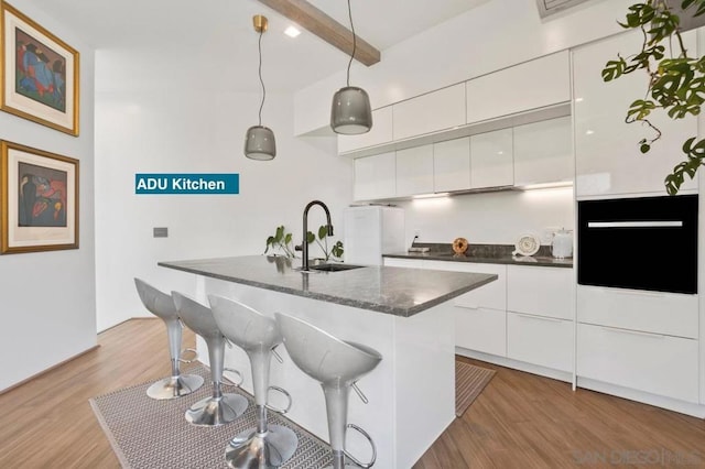 kitchen with pendant lighting, light hardwood / wood-style floors, sink, beam ceiling, and white cabinetry