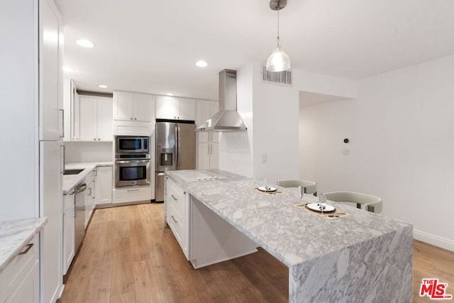 kitchen featuring white cabinets, stainless steel appliances, wall chimney range hood, and light wood-type flooring