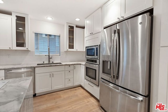 kitchen featuring light stone countertops, appliances with stainless steel finishes, sink, light hardwood / wood-style flooring, and white cabinets