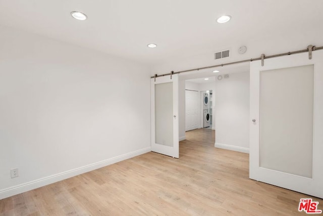 unfurnished room featuring a barn door, light wood-type flooring, and stacked washer and clothes dryer