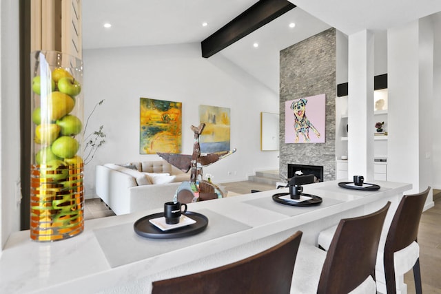 interior space with beam ceiling, hardwood / wood-style flooring, high vaulted ceiling, a kitchen bar, and a fireplace