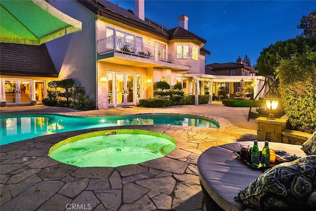 pool at twilight featuring a patio, an in ground hot tub, and french doors