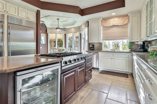 kitchen with ceiling fan, wine cooler, a tray ceiling, appliances with stainless steel finishes, and decorative backsplash