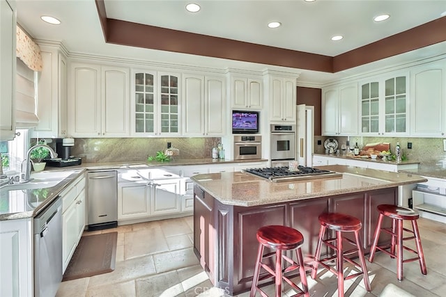 kitchen with a breakfast bar, light stone counters, a kitchen island, stainless steel appliances, and backsplash