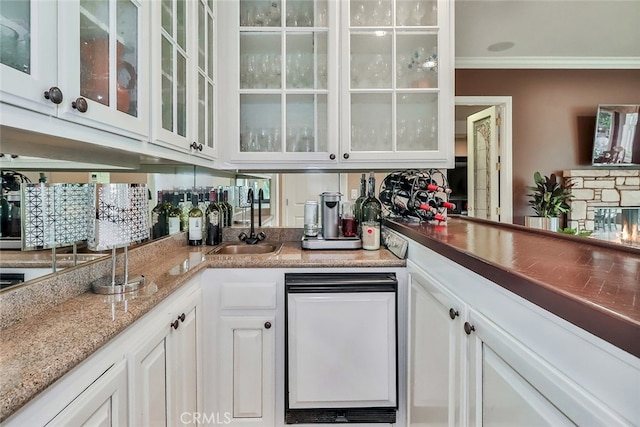 bar with light stone counters, sink, white cabinets, a fireplace, and crown molding