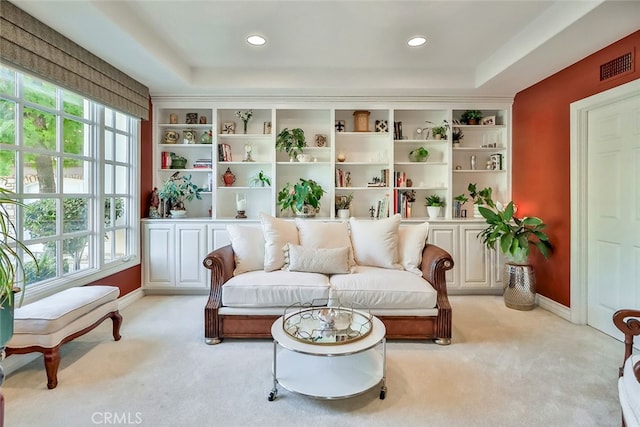 living area featuring light colored carpet, a tray ceiling, and a wealth of natural light