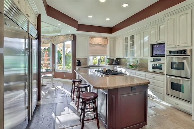 kitchen featuring a kitchen island, a kitchen breakfast bar, backsplash, a raised ceiling, and appliances with stainless steel finishes