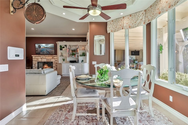 tiled dining space with crown molding, a stone fireplace, and ceiling fan