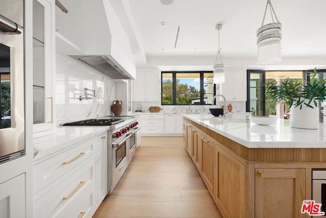 kitchen featuring light wood-type flooring, light stone counters, double oven range, white cabinetry, and a large island