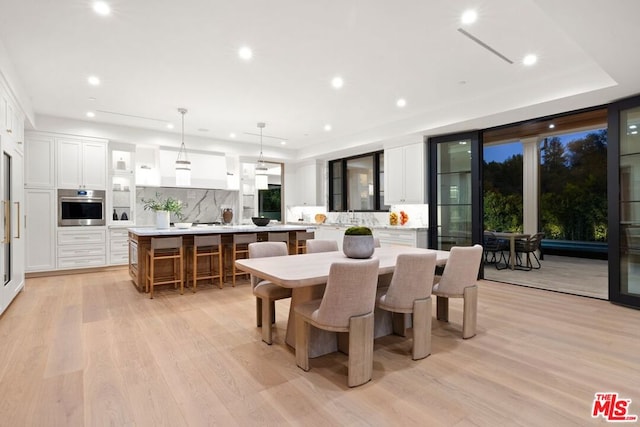 dining room with a tray ceiling, light hardwood / wood-style flooring, and sink