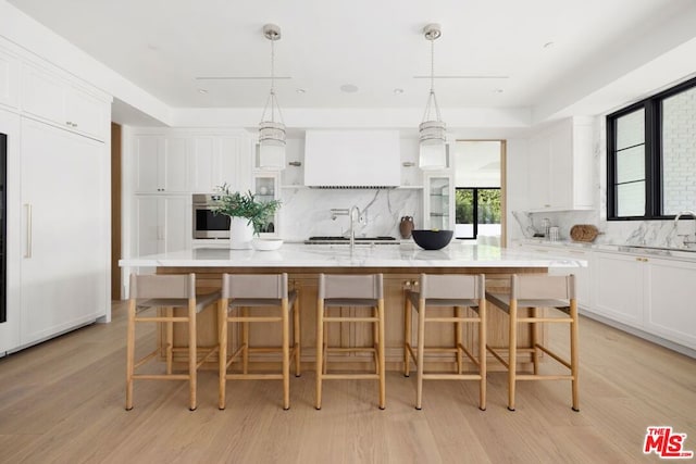 kitchen featuring decorative light fixtures, white cabinetry, a large island, and stainless steel oven