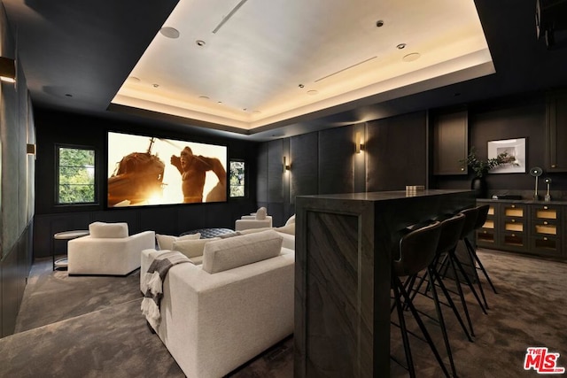 cinema room with dark colored carpet, bar area, and a tray ceiling