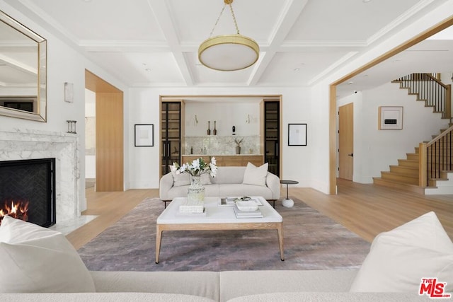 living room with light wood-type flooring, coffered ceiling, crown molding, a premium fireplace, and beamed ceiling