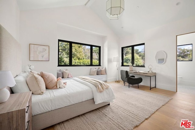 bedroom featuring beamed ceiling, light wood-type flooring, high vaulted ceiling, and connected bathroom