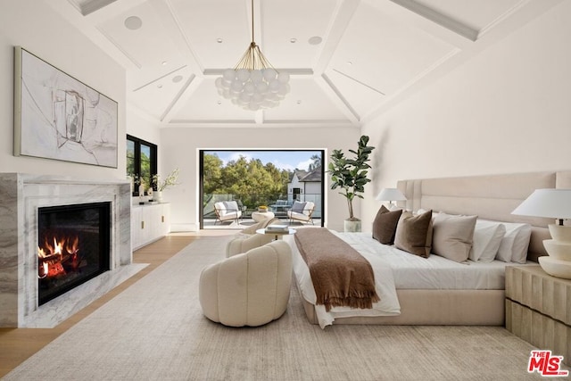 bedroom with an inviting chandelier, light hardwood / wood-style flooring, lofted ceiling, and a premium fireplace